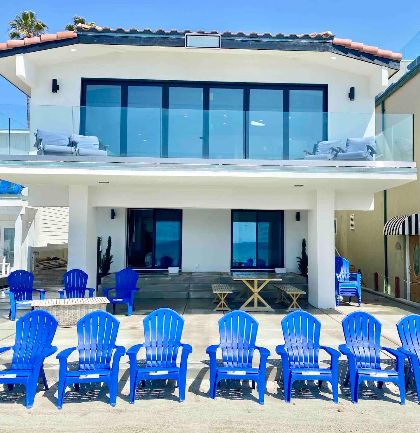 The beach house from the sand, blue Adirondack chairs lined up out front